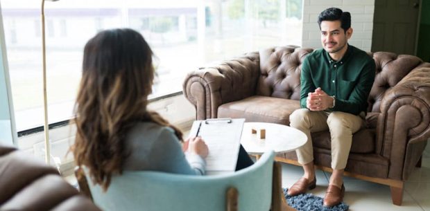 Male Professional Seeking Advice From Therapist At Office Businessman listening to female counselor during therapy session while sitting in office